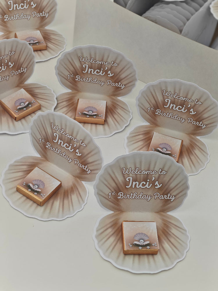 Decorative shell-shaped invitations for Inci's birthday party on a white surface.
