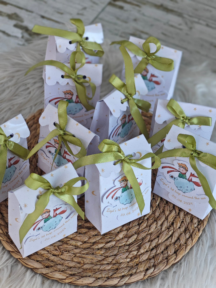 Small white boxes with green ribbons on a woven mat
