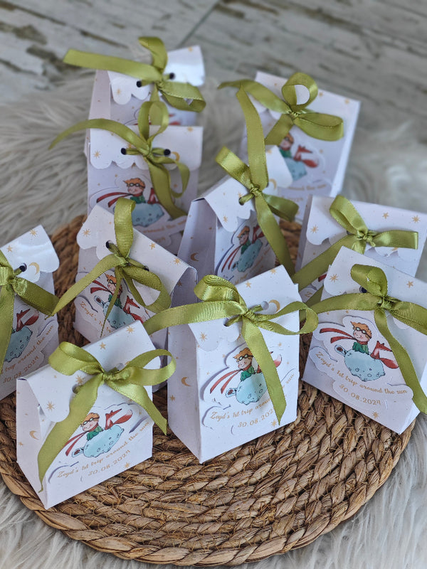 Small white boxes with green ribbons on a woven mat