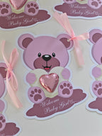 Sticker of a purple teddy bear holding a heart with 'Welcome Baby Girl' text on a light background.