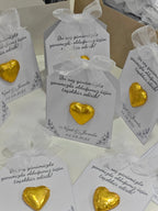 Gold heart-shaped candies in clear bags with white ribbons on a white surface.