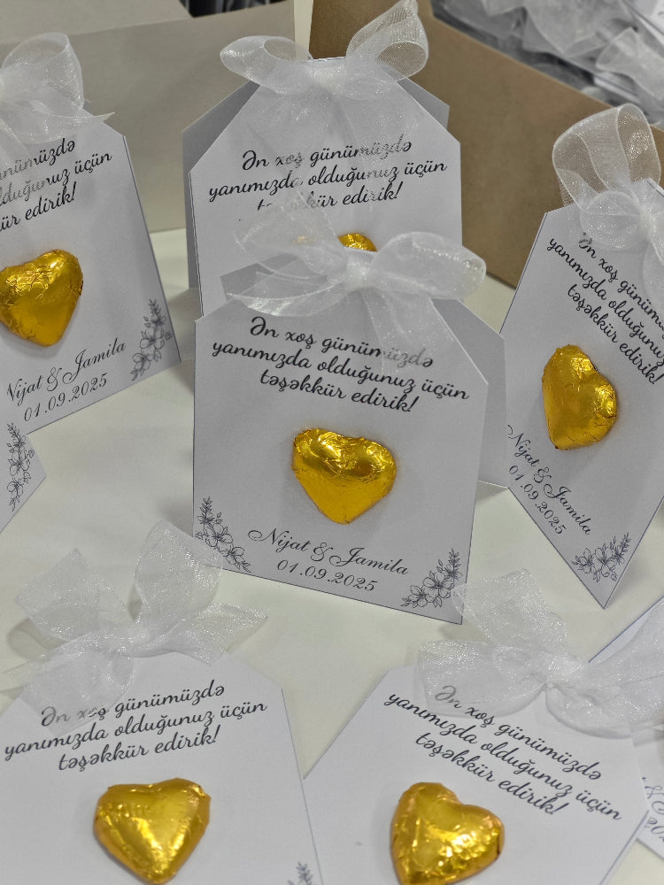 Gold heart-shaped candies in clear bags with white ribbons on a white surface.