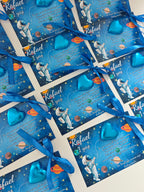 Blue gift bags with space-themed design and blue ribbons on a white background