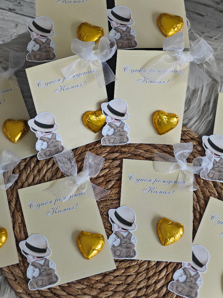 Gold heart-shaped earrings with small hats on cards, placed on a textured surface.