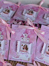 Pink party favor bags with princess design and ribbons on a wooden surface.