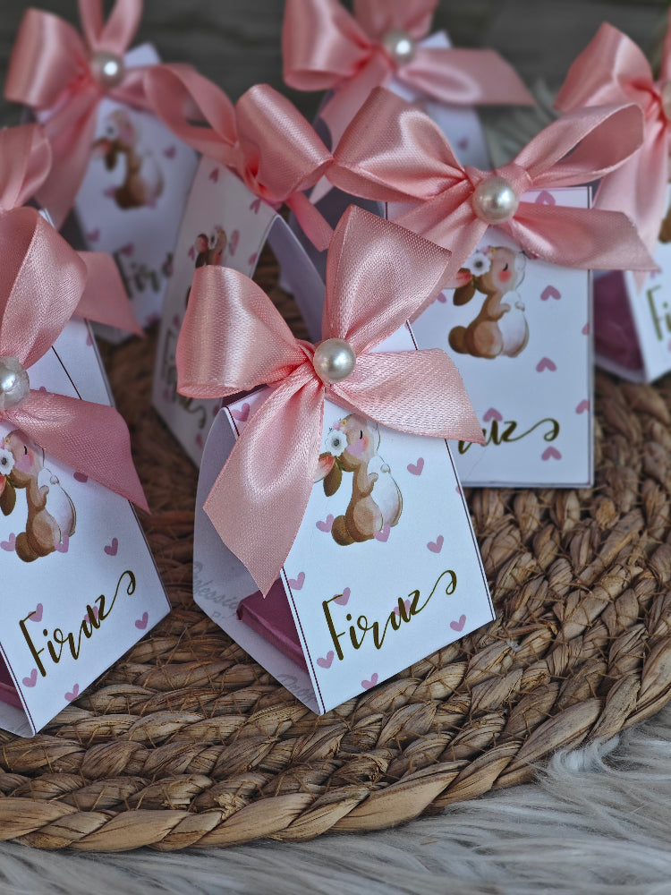 Small boxes with pink ribbons and teddy bear designs on a woven surface