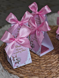 Two pink gift boxes with ribbons on a woven surface