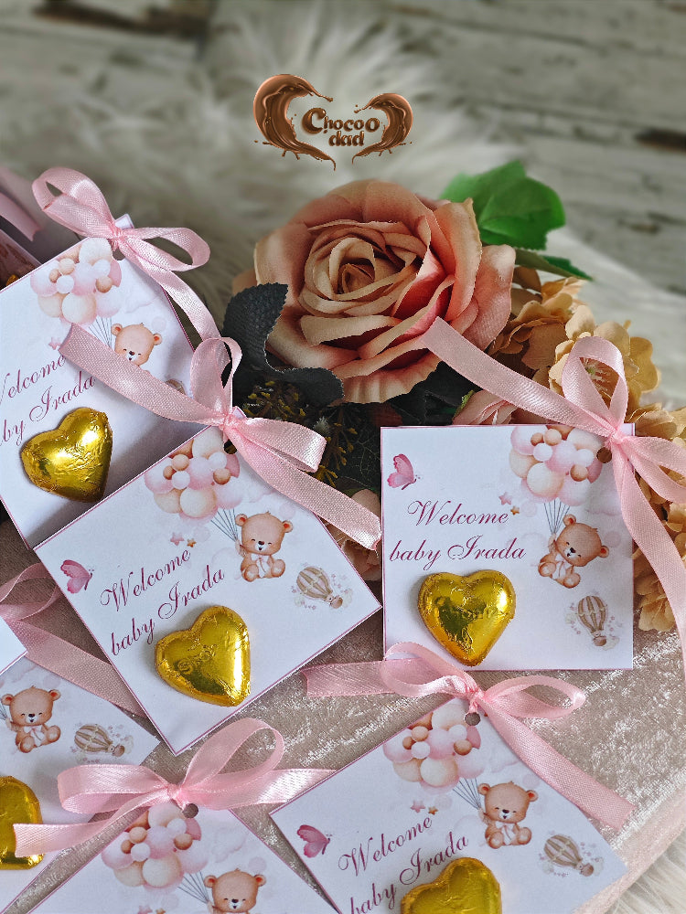 Gold heart-shaped chocolates with pink ribbons and 'Welcome baby' cards on a decorative background.