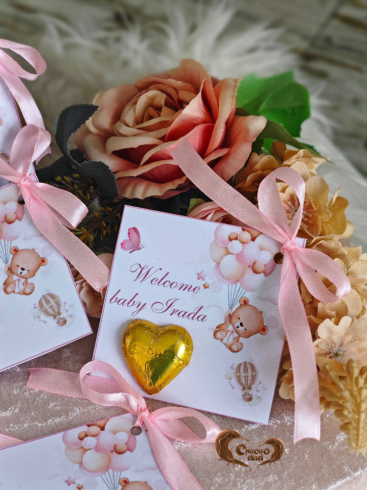 Bouquet of flowers with a pink ribbon, baby shower card, and chocolate heart on a textured surface.