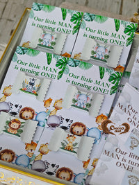 Party favor bags with jungle-themed designs and text 'Our little MAN is turning ONE!' on a wooden surface.
