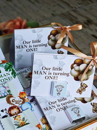 Party favor boxes with 'Our little MAN is turning ONE!' text and decorative ribbons.